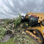 An excavator pulling at fallen branches