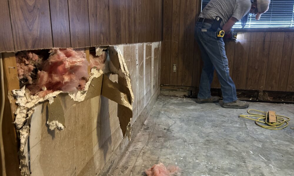 A room with wooden wall panels exposing insulation as a result of storm damage
