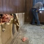 A room with wooden wall panels exposing insulation as a result of storm damage