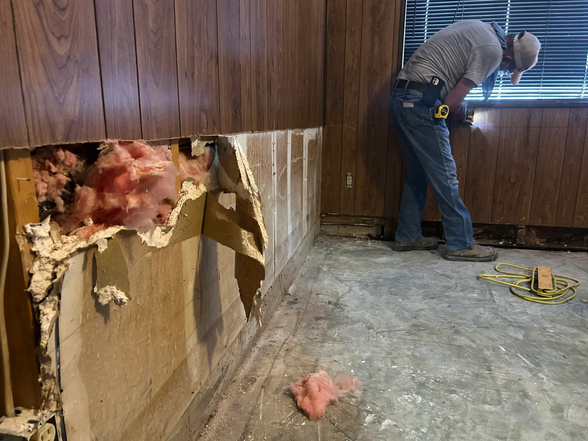 A room with wooden wall panels exposing insulation as a result of storm damage