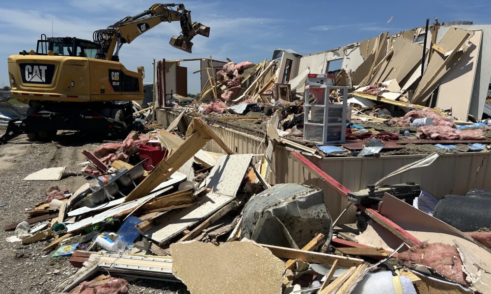 Debris from tornado damage is being cleaned up by an excavator