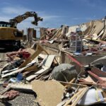 Debris from tornado damage is being cleaned up by an excavator