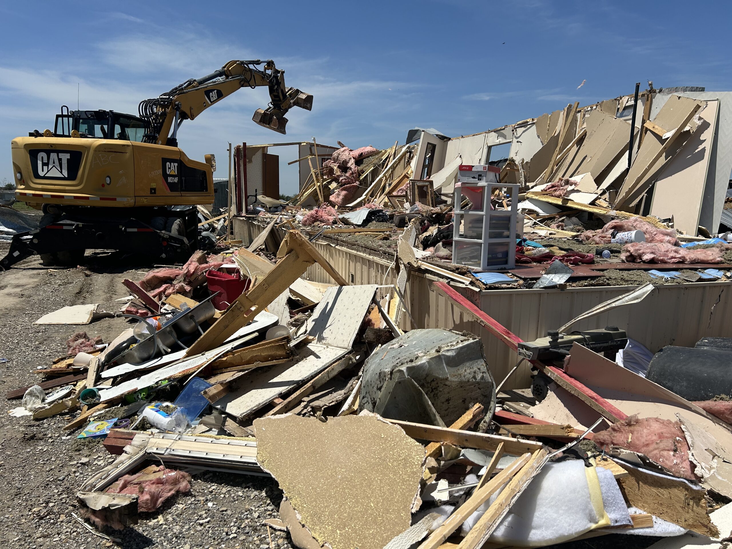 Debris from tornado damage is being cleaned up by an excavator