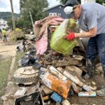 A man emptying a green bin onto a pile of debris